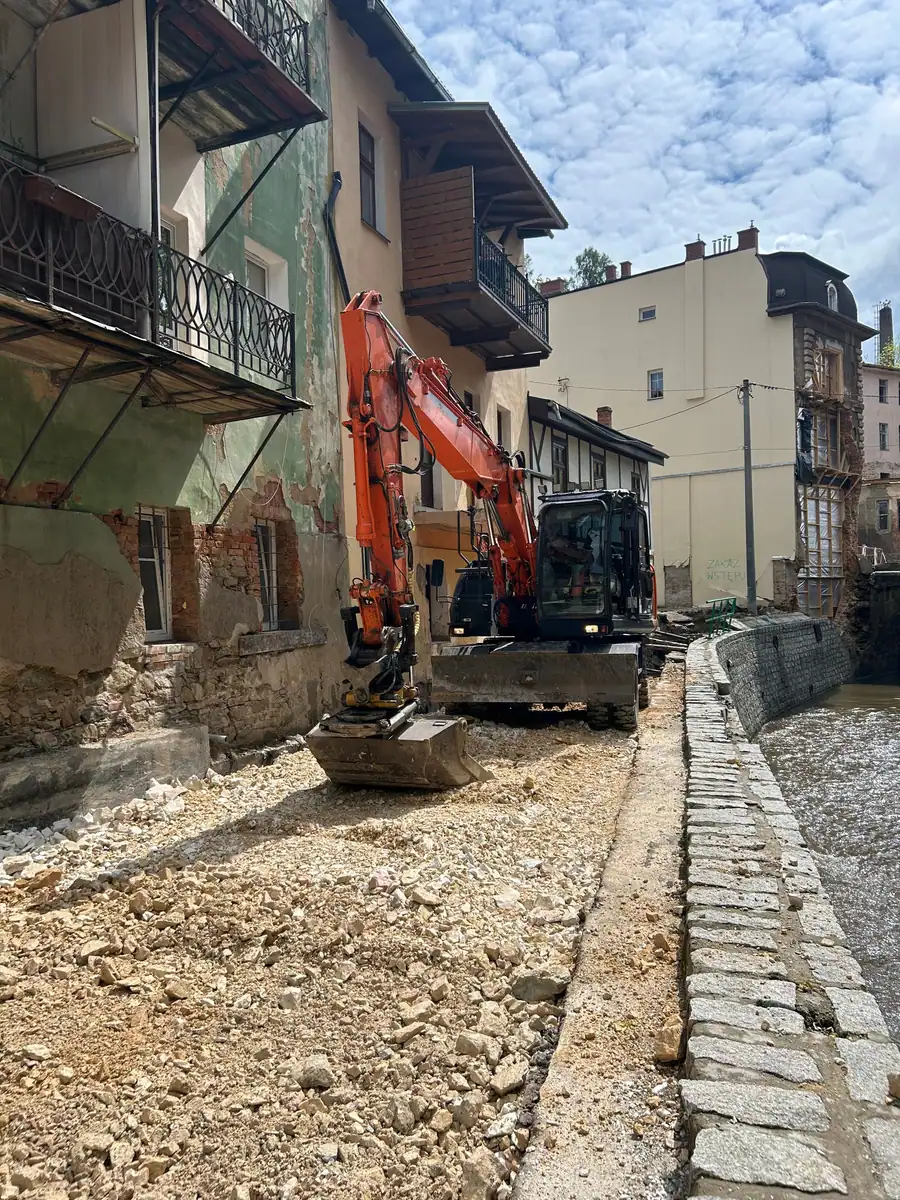 Koparka kołowa Hitachi Zaxis 140W układa tłuczeń w wąskiej uliczce nad murem koryta rzeki