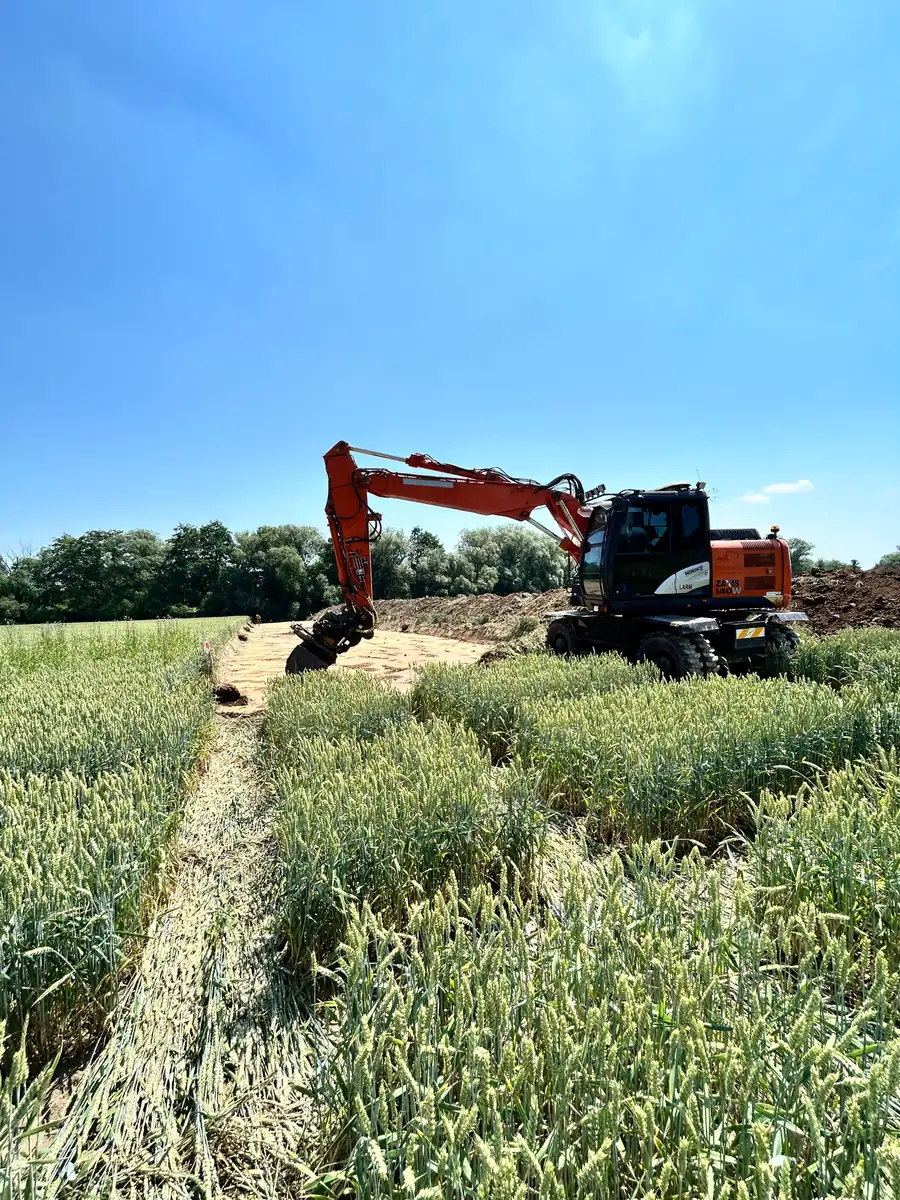 Koparka kołowa Hitachi Zaxis 140W przy pasie robót przecinającym pole zboża