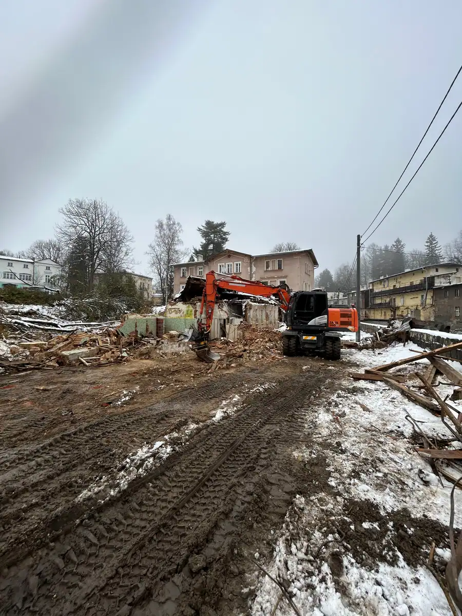 Plac po wyburzonym budynku z koparką kołową Hitachi przy resztkach murów
