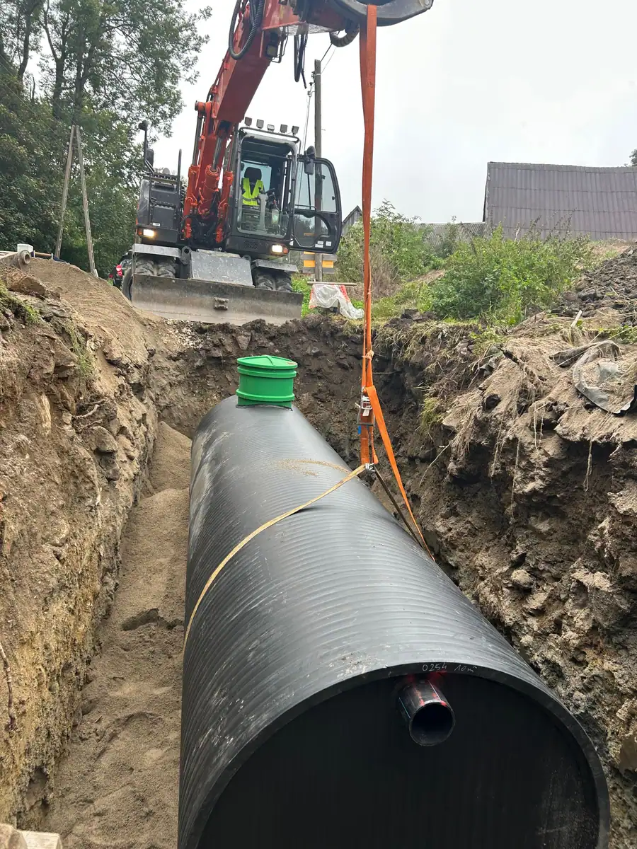 Koparka kołowa Hitachi Zaxis 140W opuszcza na pasach zbiornik z kominem rewizyjnym do wykopu