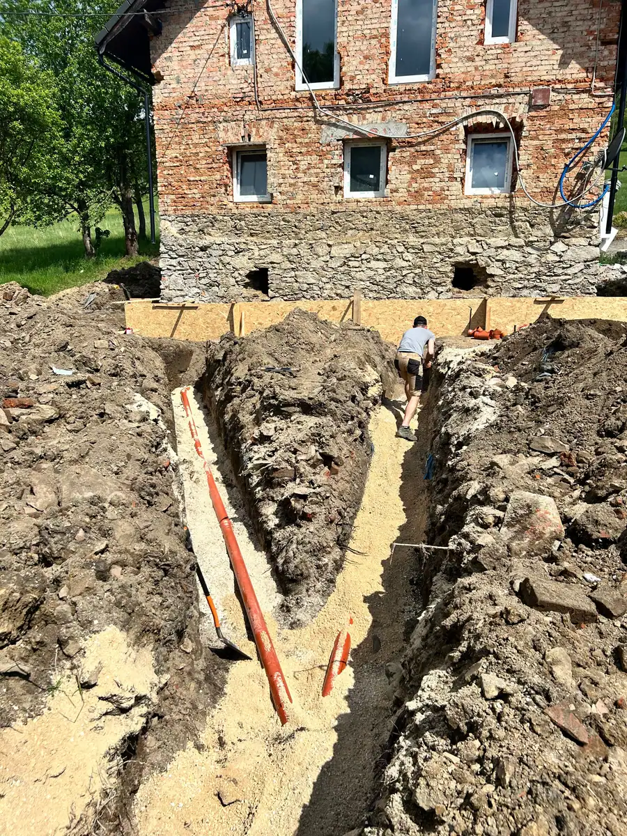 Głęboki wykop pod przyłącze kanalizacyjne wzdłuż kamiennego muru starego domu, rury PVC w dnie